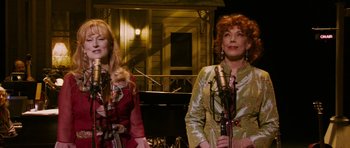 Movie still from “A Prairie Home Companion” (2006), directed by Robert Altman – A couple of women standing next to each other on a stage with microphones; Medium shot, High angle