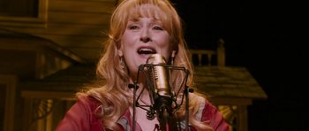 Movie still from “A Prairie Home Companion” (2006), directed by Robert Altman – A woman singing into a microphone in front of an audience; Close Up shot, Low angle