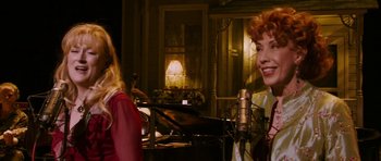 Movie still from “A Prairie Home Companion” (2006), directed by Robert Altman – Two women are singing in front of a microphone; Medium shot, Over the shoulder angle