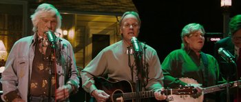 Movie still from “A Prairie Home Companion” (2006), directed by Robert Altman – An older man playing an acoustic guitar in front of a group of people; Medium shot, Low angle