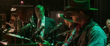 Movie still from “A Prairie Home Companion” (2006), directed by Robert Altman – A group of men in suits and hats are playing guitar; Medium shot, Over the shoulder angle