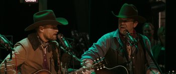Movie still from “A Prairie Home Companion” (2006), directed by Robert Altman – A couple of men in cowboy hats playing a guitar; Medium shot, Over the shoulder angle