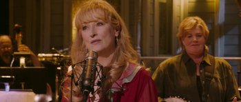Movie still from “A Prairie Home Companion” (2006), directed by Robert Altman – A woman with long blonde hair is singing into a microphone; Close Up shot, Over the shoulder angle