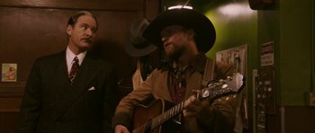 Movie still from “A Prairie Home Companion” (2006), directed by Robert Altman – A man in a cowboy hat playing a guitar; Medium shot, Over the shoulder angle