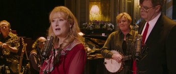 Movie still from “A Prairie Home Companion” (2006), directed by Robert Altman – Two women sing in front of a piano and a guitar; Medium shot, Over the shoulder angle