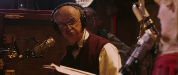 Movie still from “A Prairie Home Companion” (2006), directed by Robert Altman – An older man wearing headphones while standing in front of a microphone; Close Up shot, Low angle