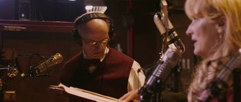 Movie still from “A Prairie Home Companion” (2006), directed by Robert Altman – An older bald man wearing headphones and a microphone; Close Up shot, Low angle