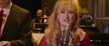 Movie still from “A Prairie Home Companion” (2006), directed by Robert Altman – A woman with long blonde hair is singing into a microphone; Close Up shot, High angle