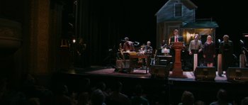 Movie still from “A Prairie Home Companion” (2006), directed by Robert Altman – A group of people sitting on a stage with microphones; Extreme Wide shot, High angle