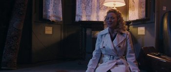 Movie still from “A Prairie Home Companion” (2006), directed by Robert Altman – A woman wearing a white trench coat sitting on the floor; Medium shot, Low angle