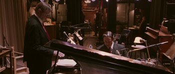 Movie still from “A Prairie Home Companion” (2006), directed by Robert Altman – A man sitting in front of a piano in a room; Medium shot, High angle