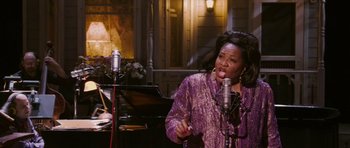 Movie still from “A Prairie Home Companion” (2006), directed by Robert Altman – A woman singing into a microphone in front of a microphone stand; Medium shot, High angle