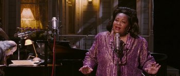 Movie still from “A Prairie Home Companion” (2006), directed by Robert Altman – An older woman singing in front of two microphones; Medium shot, High angle