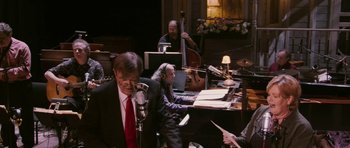 Movie still from “A Prairie Home Companion” (2006), directed by Robert Altman – A group of people sitting at a table with musical instruments; Medium shot, High angle