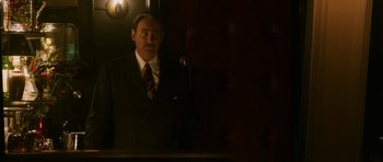 Movie still from “A Prairie Home Companion” (2006), directed by Robert Altman – A man standing in front of a microphone in a suit; Medium shot, Over the shoulder angle