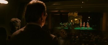 Movie still from “A Prairie Home Companion” (2006), directed by Robert Altman – A man in a suit is watching a band perform on a stage; Extreme Wide shot, Over the shoulder angle