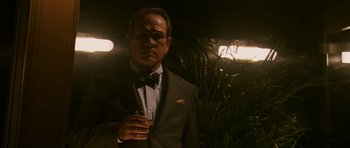 Movie still from “A Prairie Home Companion” (2006), directed by Robert Altman – A man in a suit and tie holding a glass of wine; Medium shot, Over the shoulder angle