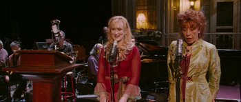 Movie still from “A Prairie Home Companion” (2006), directed by Robert Altman – A woman in a red dress singing into a microphone; Medium shot, High angle