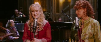 Movie still from “A Prairie Home Companion” (2006), directed by Robert Altman – A woman in a red dress singing into a microphone; Medium shot, Over the shoulder angle