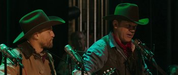 Movie still from “A Prairie Home Companion” (2006), directed by Robert Altman – Two men in cowboy hats sing into microphones; Medium shot, Over the shoulder angle