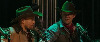 Movie still from “A Prairie Home Companion” (2006), directed by Robert Altman – Two men in green hats sing into microphones; Medium shot, Over the shoulder angle