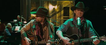 Movie still from “A Prairie Home Companion” (2006), directed by Robert Altman – A man in a cowboy hat playing an acoustic guitar; Medium shot, Over the shoulder angle