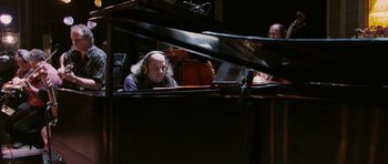 Movie still from “A Prairie Home Companion” (2006), directed by Robert Altman – A man with headphones sitting in front of a grand piano; Medium shot, High angle