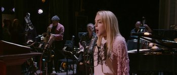 Movie still from “A Prairie Home Companion” (2006), directed by Robert Altman – A woman singing into a microphone in front of a group of people; Medium shot, Over the shoulder angle