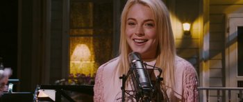 Movie still from “A Prairie Home Companion” (2006), directed by Robert Altman – A beautiful young lady holding a microphone and smiling for the camera; Close Up shot, Over the shoulder angle