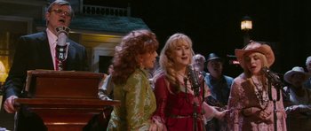 Movie still from “A Prairie Home Companion” (2006), directed by Robert Altman – Two women singing in front of a microphone; Medium shot, Over the shoulder angle