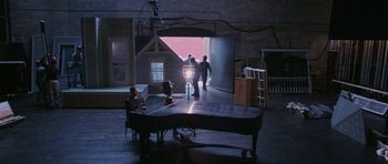Movie still from “A Prairie Home Companion” (2006), directed by Robert Altman – Two people are standing in a room behind a piano; Extreme Wide shot, High angle