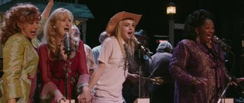 Movie still from “A Prairie Home Companion” (2006), directed by Robert Altman – A woman in a cowboy hat singing into a microphone; Medium shot, Over the shoulder angle