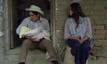 Movie still from “Alambrista!” (1977), directed by Robert M. Young – A man and a woman sitting next to each other holding a baby; Medium shot, High angle