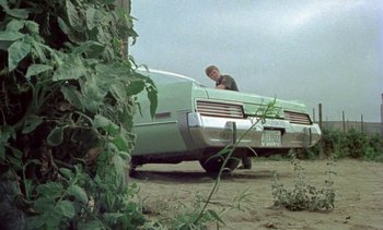 Movie still from “Alambrista!” (1977), directed by Robert M. Young – A man standing next to an old green car; Wide shot, Low angle