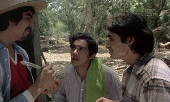 Movie still from “Alambrista!” (1977), directed by Robert M. Young – Two young men are talking to each other in a wooded area; Medium shot, Over the shoulder angle