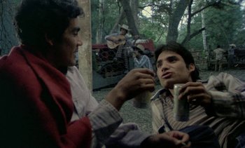 Movie still from “Alambrista!” (1977), directed by Robert M. Young – Two young men sitting on the ground with a drink; Medium shot, Low angle