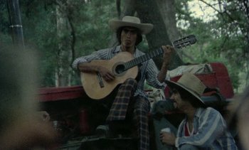 Movie still from “Alambrista!” (1977), directed by Robert M. Young – A man playing a guitar while sitting next to another man; Medium shot, Low angle