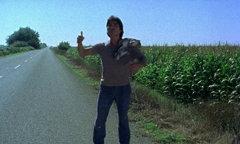 Movie still from “Alambrista!” (1977), directed by Robert M. Young – A man standing on the side of a road holding a dog; Wide shot, Low angle
