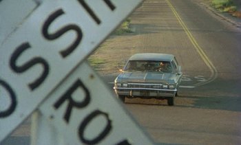Movie still from “Alambrista!” (1977), directed by Robert M. Young – A car driving down a street next to a street sign; Wide shot, High angle