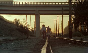 Movie still from “Alambrista!” (1977), directed by Robert M. Young – Two people are walking on the railroad tracks at sunset; Wide shot, Low angle