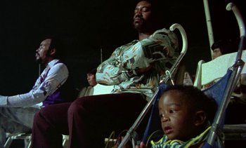 Movie still from “Alambrista!” (1977), directed by Robert M. Young – A man sitting in a chair next to a child; Medium shot, Low angle