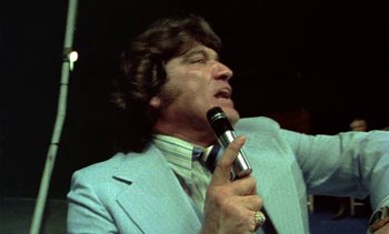 Movie still from “Alambrista!” (1977), directed by Robert M. Young – A man in a suit and tie holding a microphone; Close Up shot, Low angle