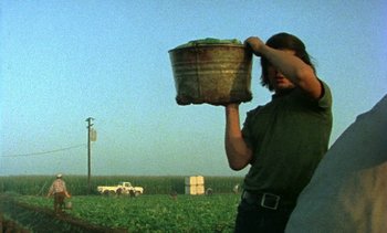Movie still from “Alambrista!” (1977), directed by Robert M. Young – A man holding a bucket in a field with a truck in the background; Medium shot, Low angle
