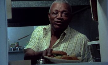 Movie still from “Alambrista!” (1977), directed by Robert M. Young – An older man sitting at a table holding a plate of food; Medium shot, Low angle