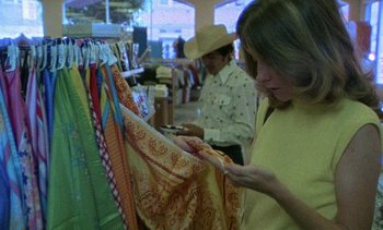 Movie still from “Alambrista!” (1977), directed by Robert M. Young – A woman looking at a scarf on a rack; Medium shot, Over the shoulder angle