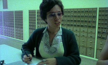 Movie still from “Alambrista!” (1977), directed by Robert M. Young – A woman writing on a piece of paper in a room; Medium shot, Low angle