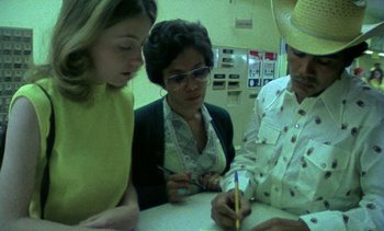 Movie still from “Alambrista!” (1977), directed by Robert M. Young – A group of people sitting at a table writing on a piece of paper; Medium shot, High angle