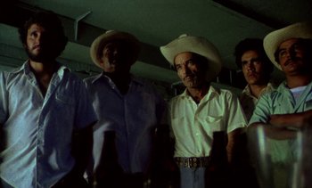 Movie still from “Alambrista!” (1977), directed by Robert M. Young – A group of men standing next to each other in a room; Medium shot, Low angle