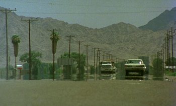Movie still from “Alambrista!” (1977), directed by Robert M. Young – Cars driving down a street in the middle of the desert; Extreme Wide shot, Low angle