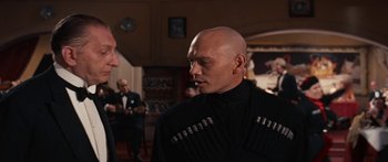 Movie still from “Anastasia” (1956), directed by Anatole Litvak – A bald man in a black shirt is talking to another man in a black suit; Close Up shot, Over the shoulder angle